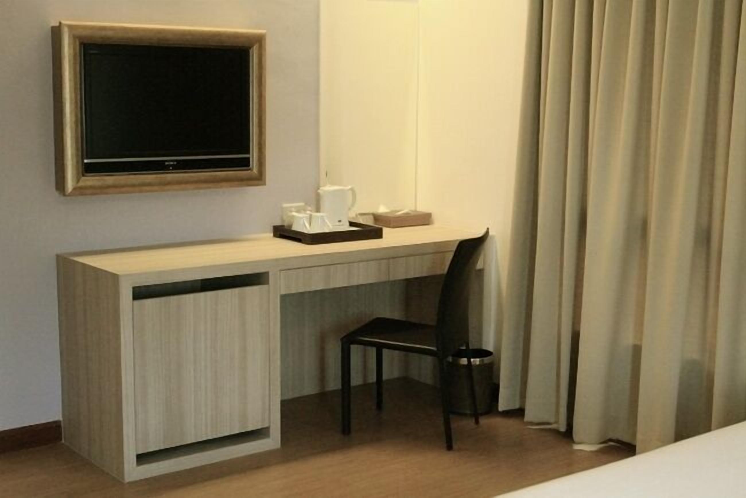 A hotel room with a wooden desk, a television, a chair, a coffee maker, and a curtain.