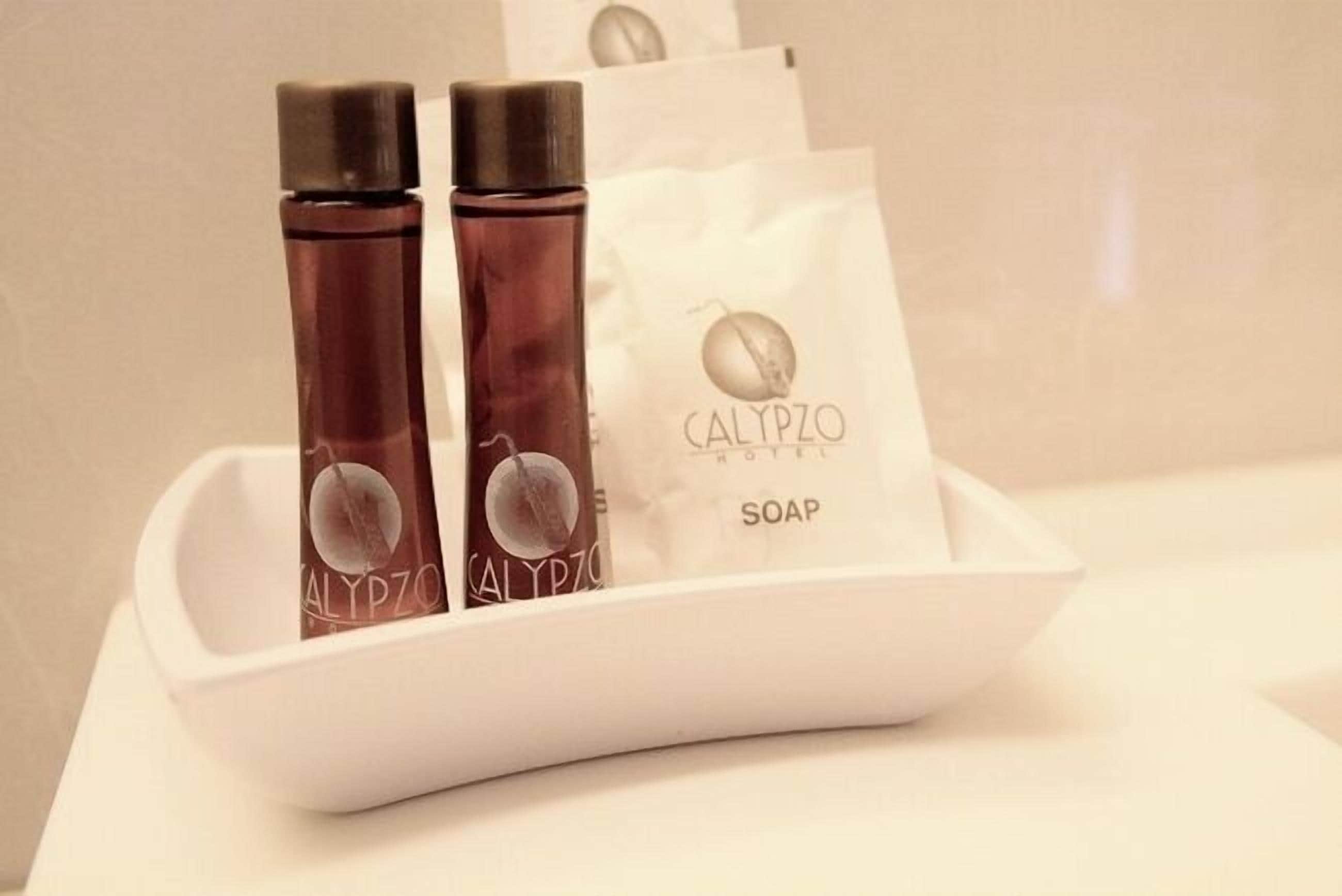 Un porte-savon blanc contenant deux flacons de savon Calypso et un pain de savon blanc.