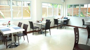 A dining area with multiple tables and chairs, large windows with wooden blinds, and a clean, tiled floor. - Calypzo 2 (Bangkok)