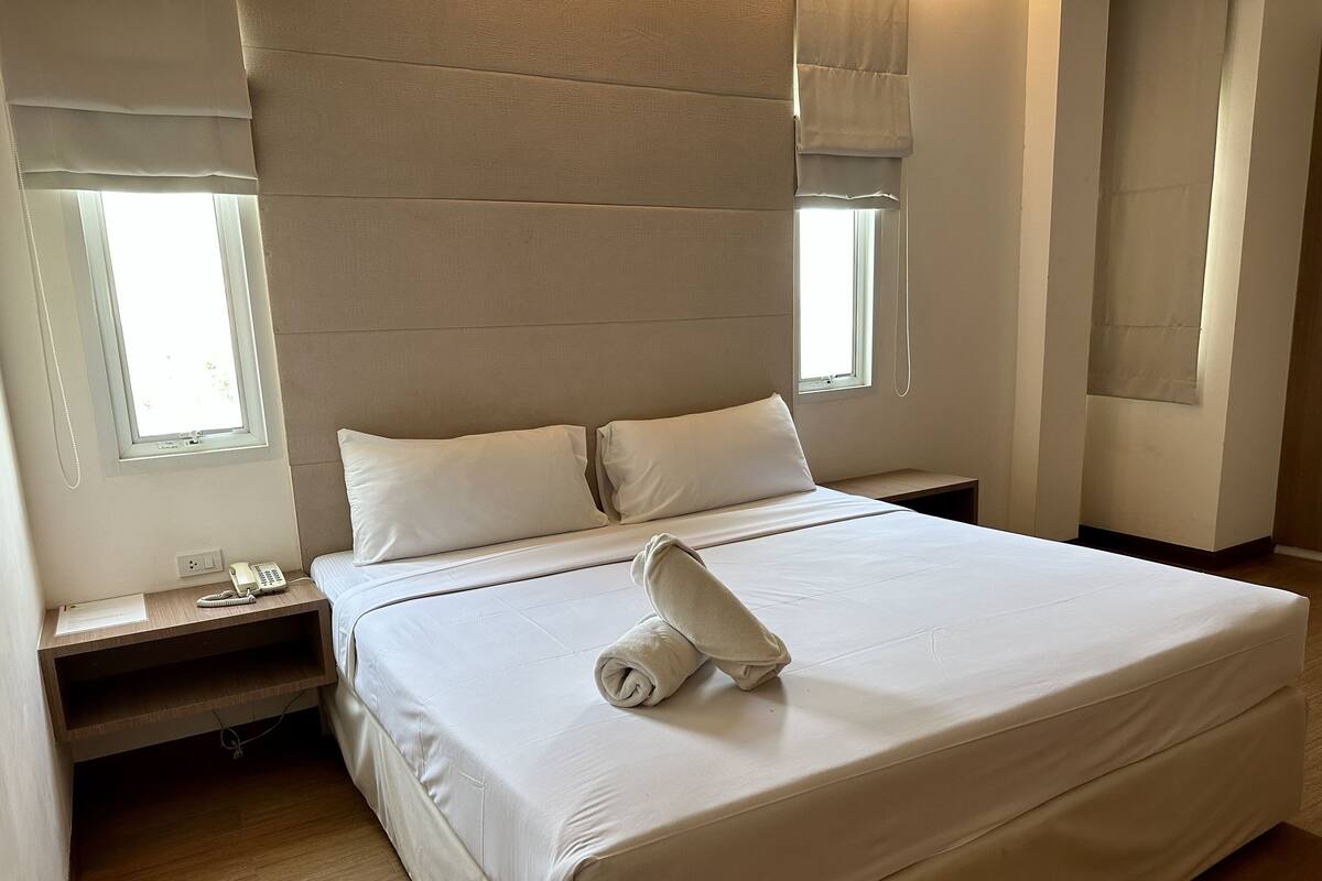 A neatly made bed with a rolled towel, a bedside phone, and a small table with a lamp.