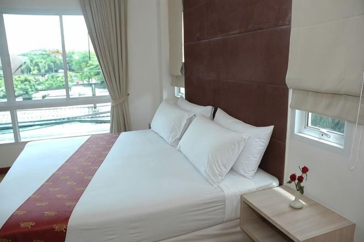 Een hotelkamer met een groot bed, een nachtkastje, een raam met gordijnen en uitzicht op groen.