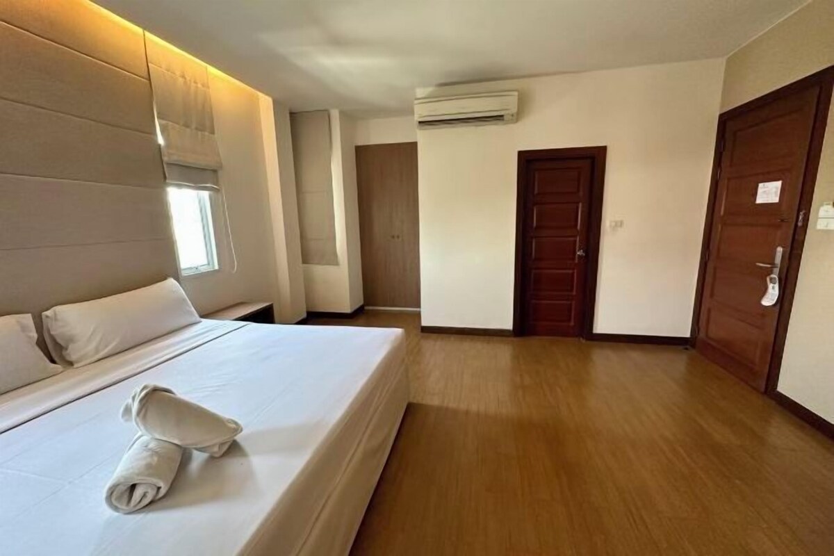 Een hotelkamer met een bed, een raam, een airconditioner en houten vloeren.