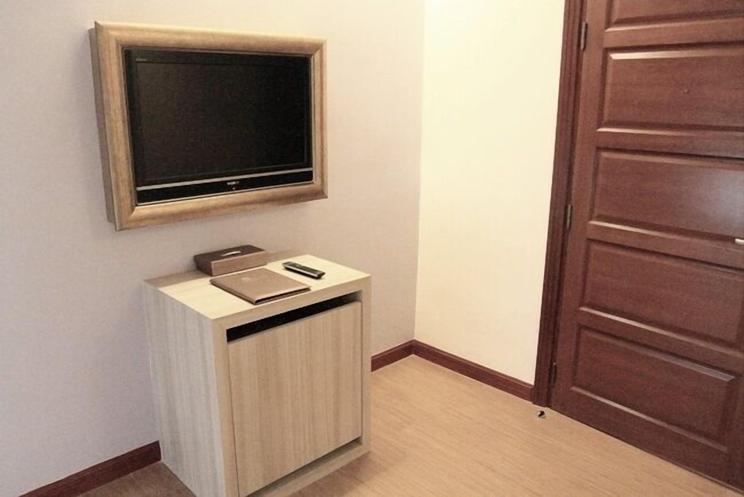 A room with a mounted television above a wooden cabinet, a door to the right, and a light-colored floor.