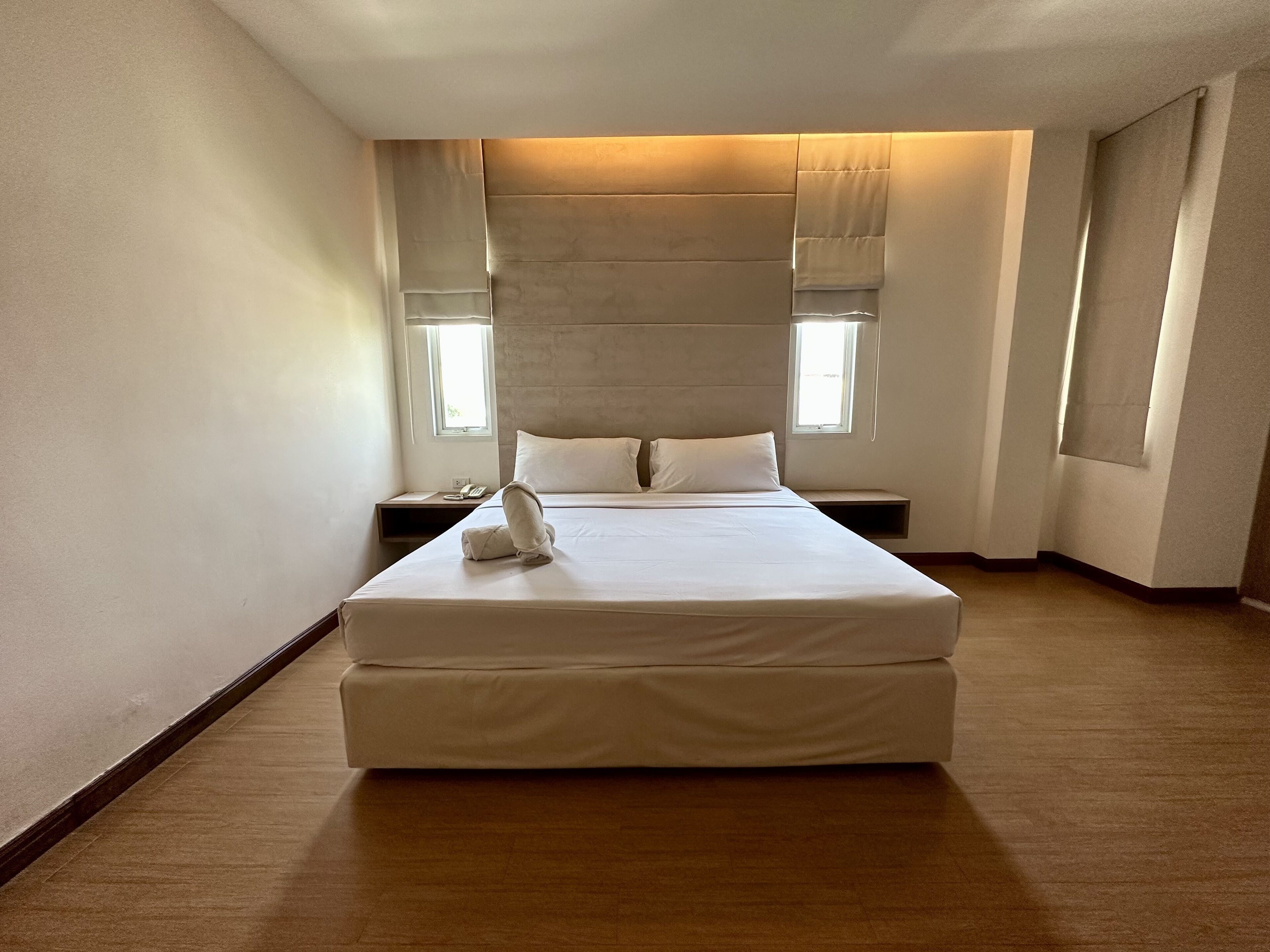 A modern hotel room with a large bed, a bedside table, and a window with curtains.