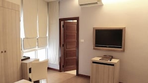 A compact room with a wooden door, a small table, a chair, a cabinet, and a mounted TV. - Calypzo 2 (Bangkok)
