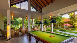 A pool table with a green felt surface, surrounded by wicker chairs and a ceiling fan.