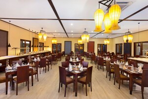 Un comedor amplio con varias mesas dispuestas para el servicio, que presenta mobiliario de madera e iluminación colgante.