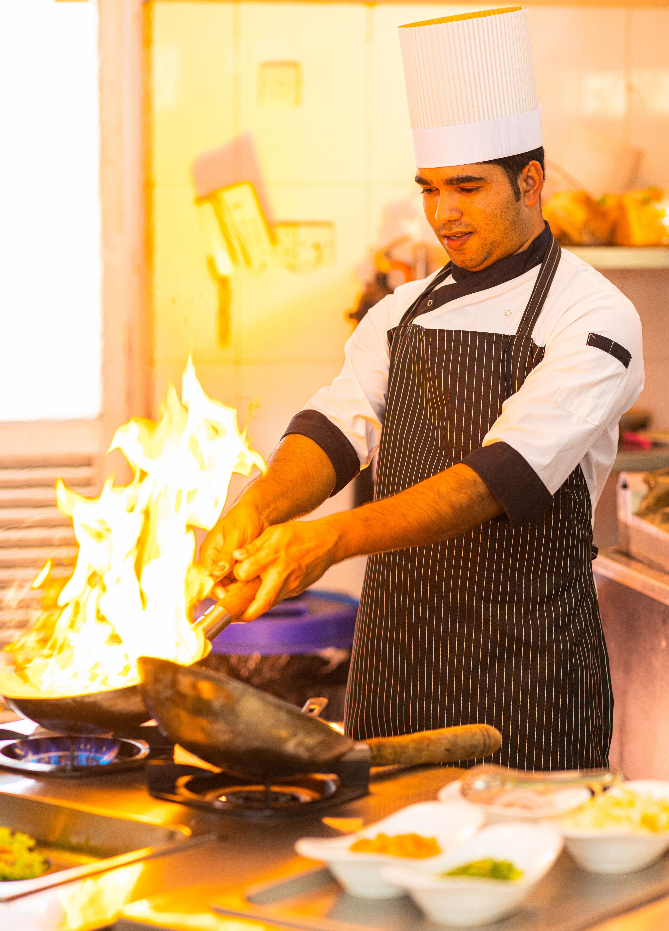 A chef preparing food with a flame on a stove.