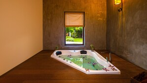 A spa room with a large bathtub, a window with a view of greenery, and a wall-mounted light fixture.