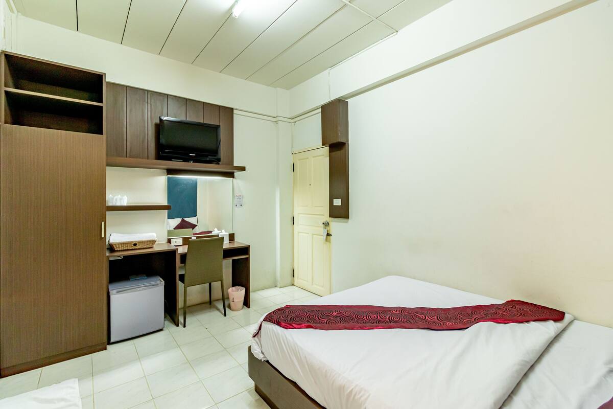 Quarto de hotel com cama, escrivaninha, cadeira, televisão e armário.
