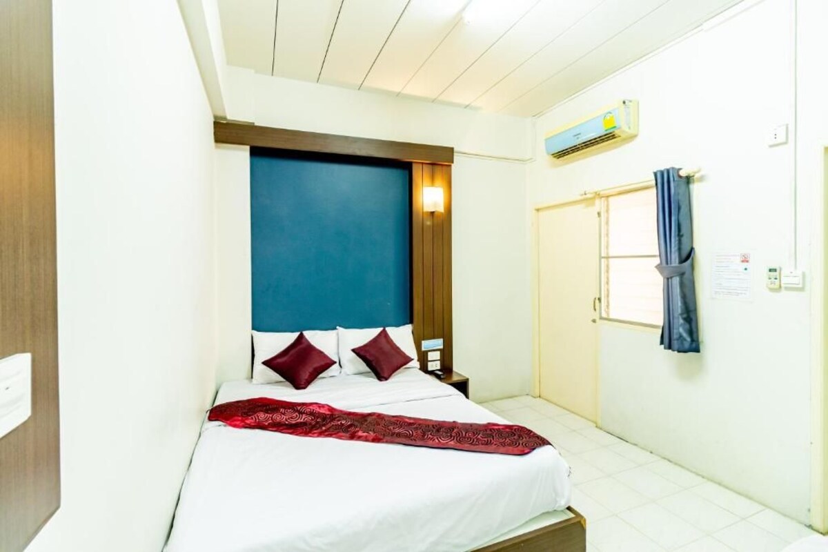 A hotel room with a bed, a nightstand, a window with curtains, and an air conditioning unit.