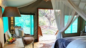 Una habitación con carpa, una cama, una mesa con lámpara y vistas al exterior.