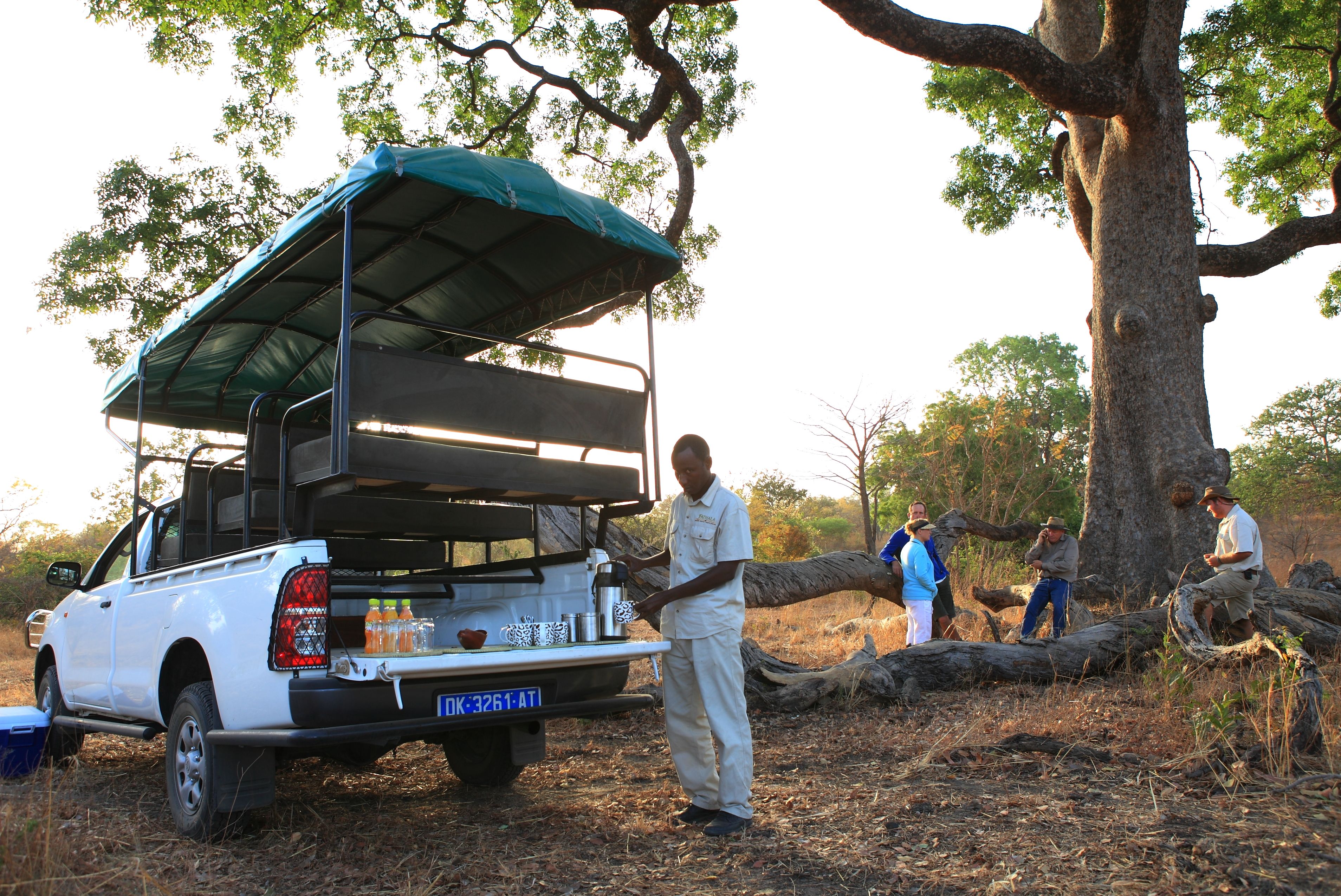 A white pickup truck with a covered cargo area, parked in a wooded area with people around.