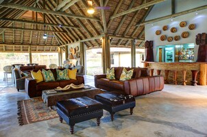 A spacious lounge with leather sofas and ottomans, a bar area with wooden decor, and a rustic ceiling.