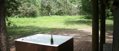 A hot tub on a wooden deck with a bottle and glass, surrounded by greenery.