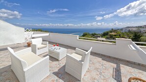 Una terraza en la azotea con muebles de mimbre, una mesa y vistas al mar.