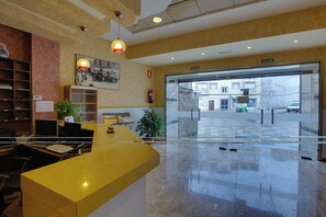 A hotel reception area with a counter, a fire extinguisher, a framed photograph, and a glass door leading outside. - Hotel Restaurante Los Chiles (Villanueva del Arzobispo)