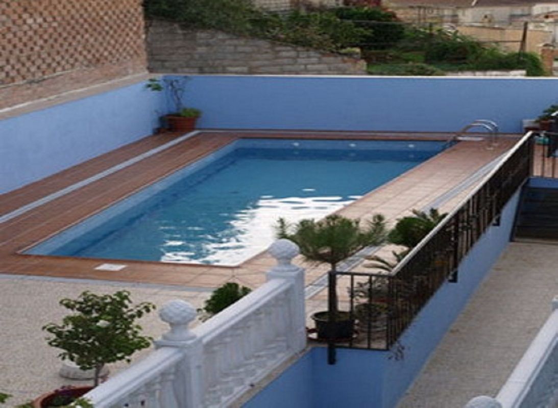 A rectangular swimming pool with a wooden deck, surrounded by a blue wall and a white balustrade.