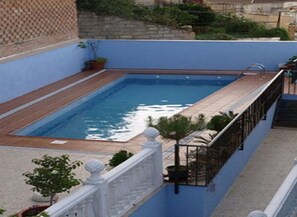 A rectangular swimming pool with a wooden deck, surrounded by a blue wall and a white balustrade. - Hotel Restaurante Los Chiles (Villanueva del Arzobispo)