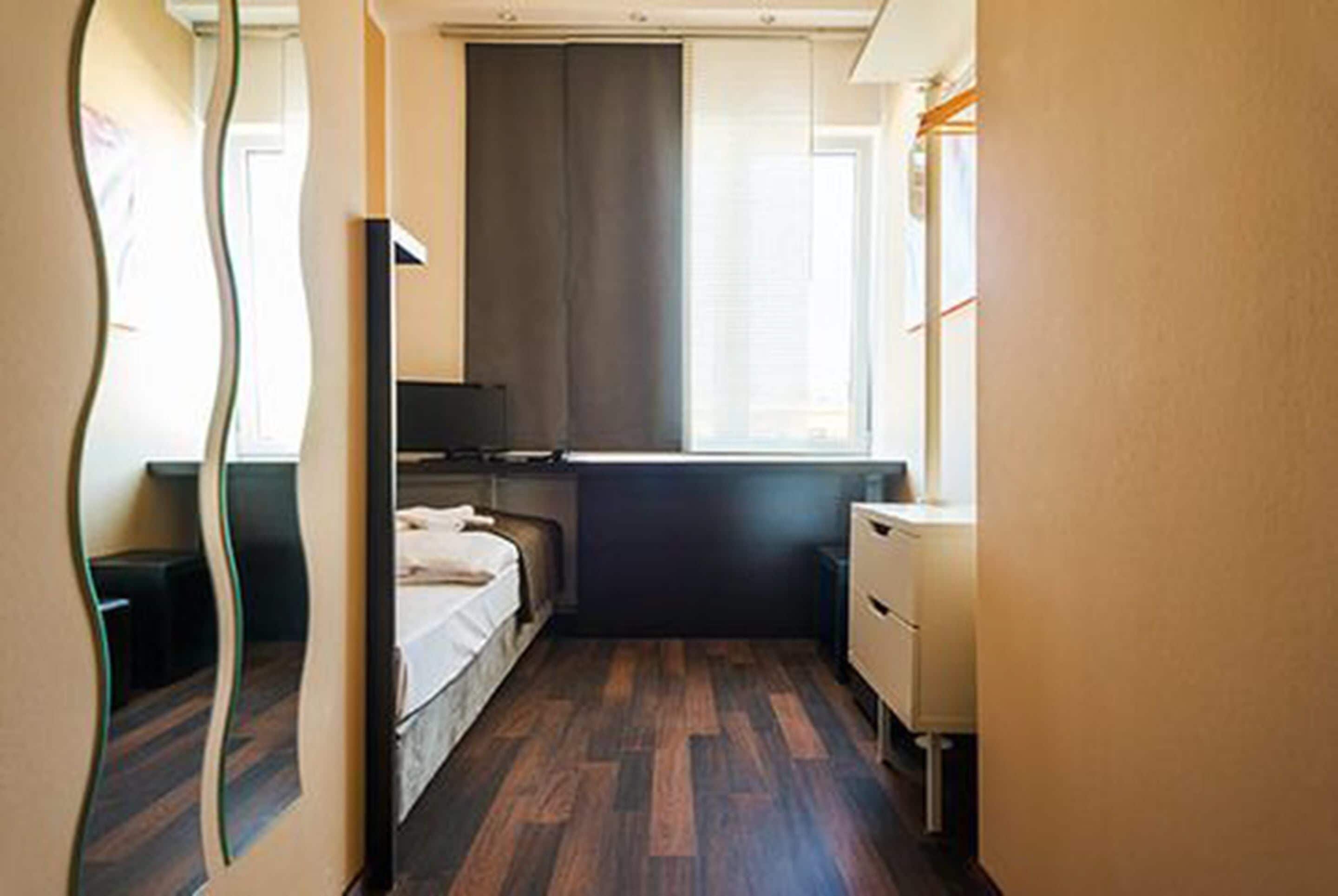 A narrow hotel room with a bed, a desk, and a window.