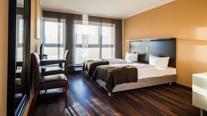 A hotel room with a bed, two bedside tables, a desk with a chair, and large windows with blinds. - Apple City Hotel (Berlin)