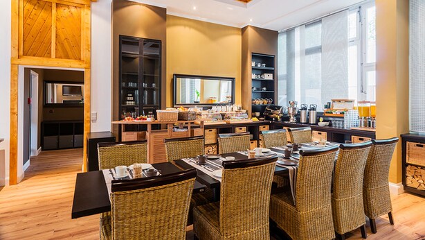 A spacious dining area with wicker chairs and a long table, a kitchen with modern appliances, and large windows providing natural light. - Apple City Hotel (Berlin)