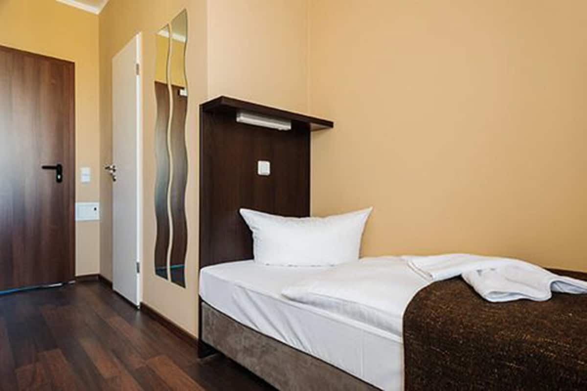 A hotel room with a bed, a wooden door, a mirror, and a light fixture above the bed.