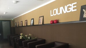 A lounge area with a row of dark brown chairs, a wall with the word "LOUNGE" and framed pictures, and a wooden floor. - Apple City Hotel (Berlin)