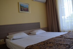 A hotel room with two beds, a headboard, a painting on the wall, and a window with curtains. - Villa Orange (Sozopol)
