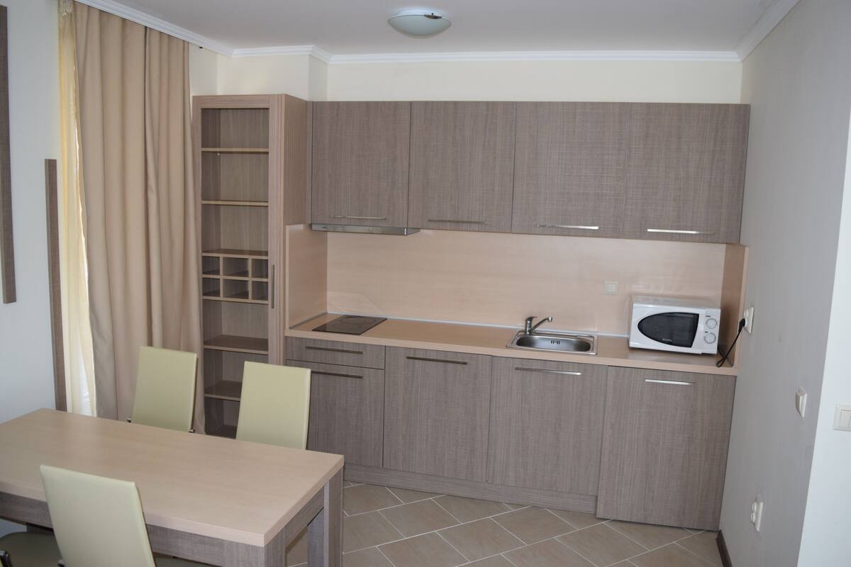 A compact kitchen with a dining table and chairs, a microwave, and a built-in shelf.