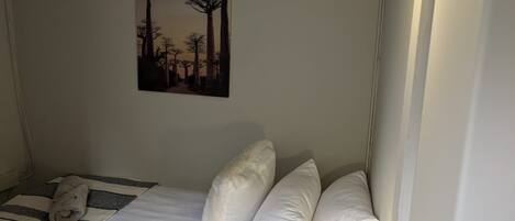 Een slaapkamer met een bed, kussens, dekbed, een aan de muur hangend schilderij en een bedlampje.