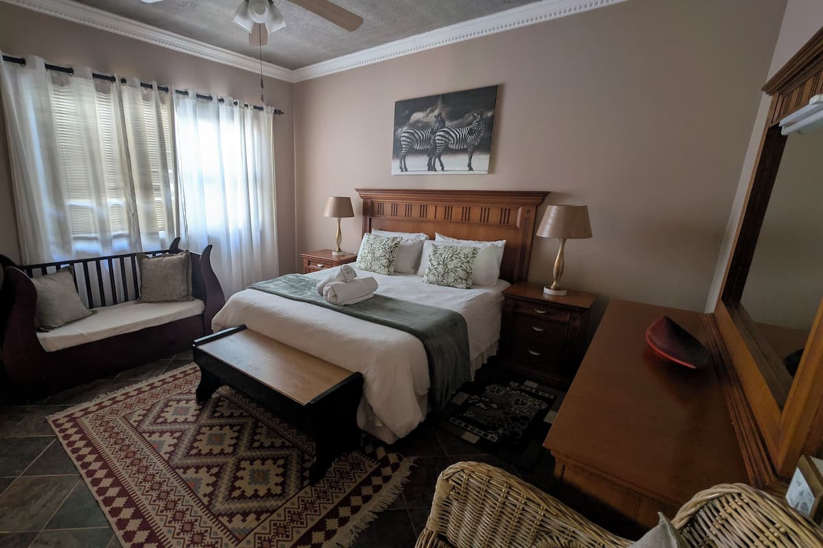 Een hotelkamer met een bed, een bankje, een bureau, een stoel, een kleed en een schilderij aan de muur.