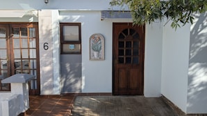Un edificio con el número 6 en la puerta, una pequeña ventana con persianas y una planta en maceta en la pared.