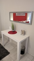 Una mesa blanca con un mantel individual rojo, una planta en maceta y un cartel motivacional.