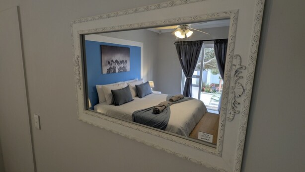 A bedroom with a bed, pillows, a blanket, a ceiling fan, and a window with curtains. - Amarachi Guesthouse (Swakopmund)