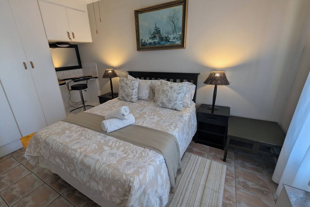 Een keurig opgeruimde slaapkamer met een bed, twee nachtkastjes, een bureau en een stoel.