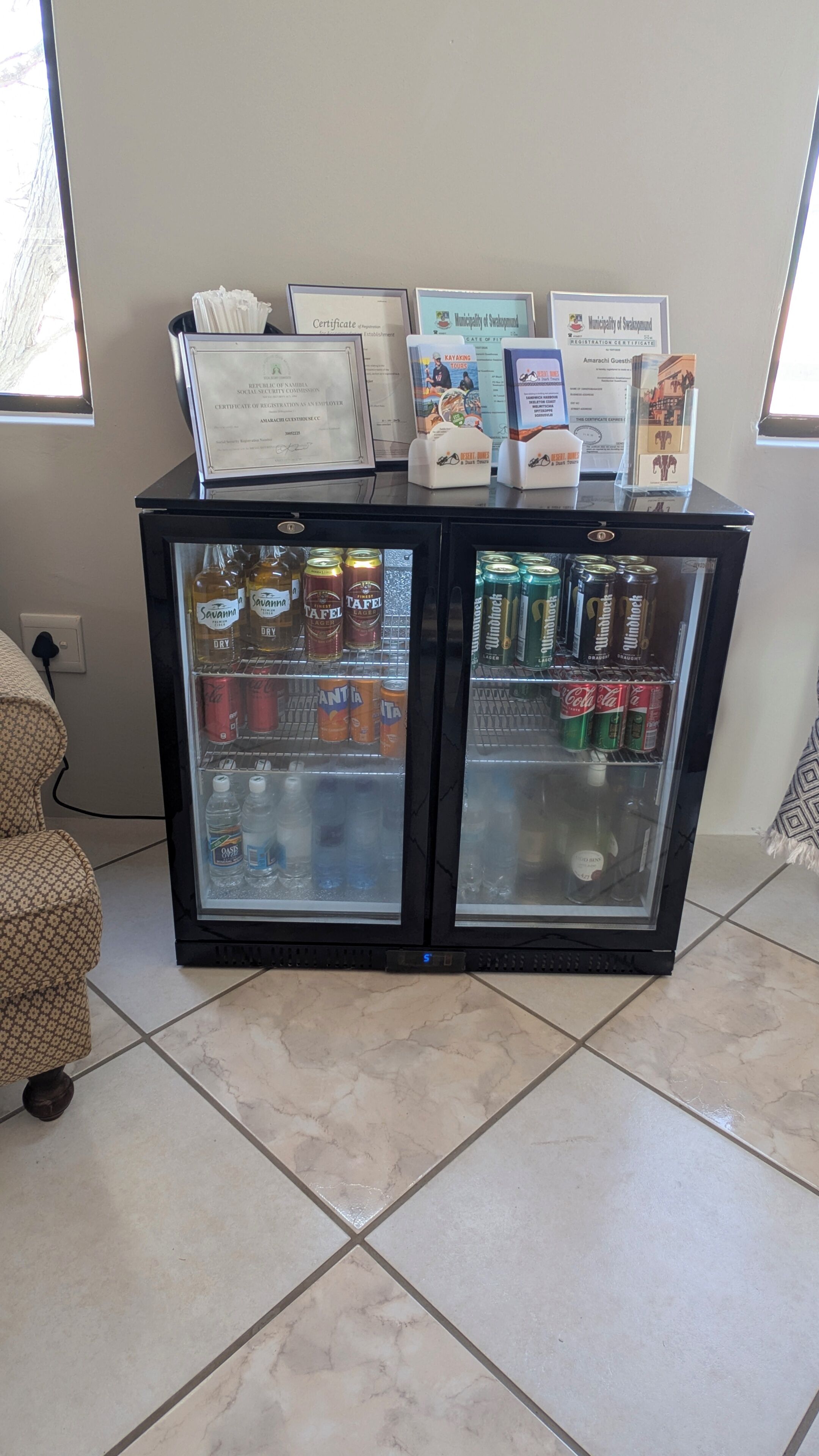 Een drankkoeler gevuld met diverse drankjes, waaronder blikjes frisdrank en flessen bier, met certificaten en informatiemapjes erboven.