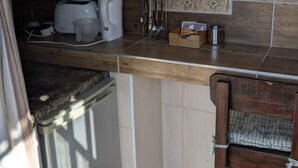 A compact kitchen with a wooden countertop, a refrigerator, a sink, and a dining area with a chair. - Amarachi Guesthouse (Swakopmund)