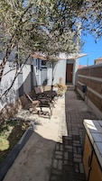 Ein Terrassenbereich im Freien mit Tisch und Stühlen, ein kleiner Garten und ein Gebäude mit einem Ziegeldach.