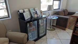 Una sala de estar con un sofá, una mesa de centro, un refrigerador con bebidas y una lámpara.