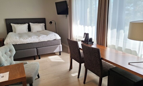 Habitación de hotel con cama, escritorio con silla, televisor montado en la pared y ventana con cortinas.