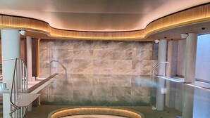 Un spa moderno con una bañera de hidromasaje curva, paredes de piedra y una barrera de cristal.