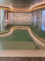 Un spa moderno con una bañera de hidromasaje curva, paredes de piedra y una barrera de cristal.