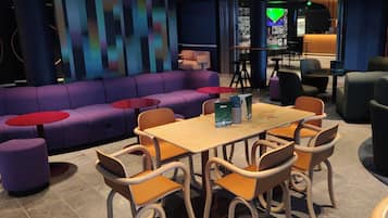 A modern lounge area with purple sofas, wooden chairs, and red tables.