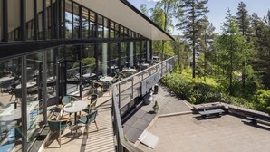 Un área de estar moderna al aire libre con mesas y sillas, con vistas a un paisaje boscoso.
