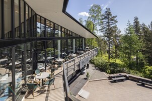Un área de estar moderna al aire libre con mesas y sillas, con vistas a un paisaje boscoso.
