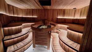 A circular seating area with a central fire feature, surrounded by wooden paneling and cushioned benches. - Hotel Majvik (Kirkkonummi)
