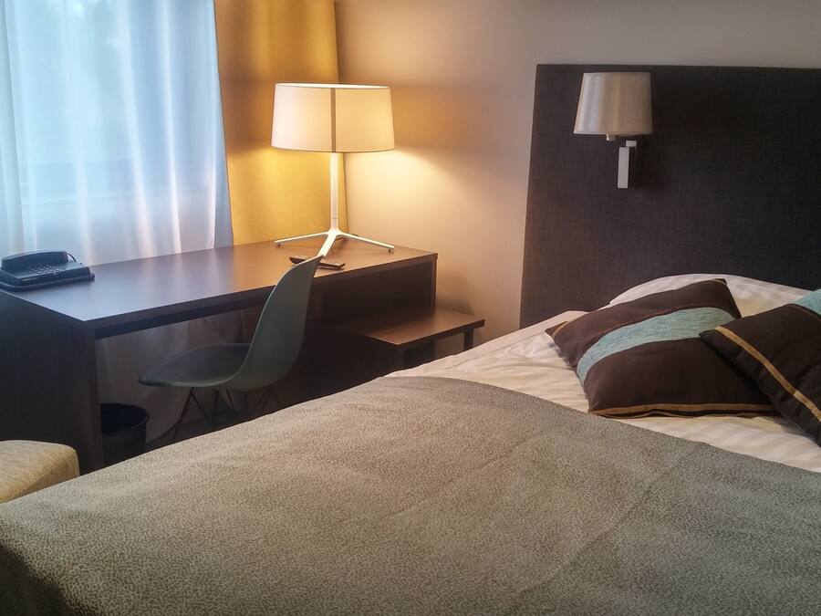 Camera d'albergo con un letto, una scrivania, una sedia, una lampada e un telefono.