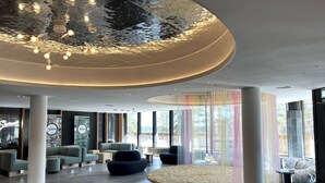 Un moderno vestíbulo de hotel con un diseño de techo único, cómodas zonas de estar y amplios ventanales con vistas al exterior.