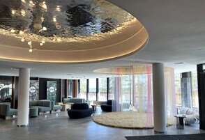 Un moderno vestíbulo de hotel con un diseño de techo único, cómodas zonas de estar y amplios ventanales con vistas al exterior.